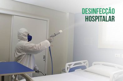 Profissional em equipamento de proteção pulverizando desinfetante em quarto hospitalar.