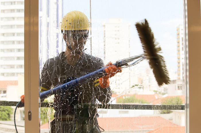 Imagem de profissional realizando limpeza externa de vidro ilustrando os riscos do trabalho em altura